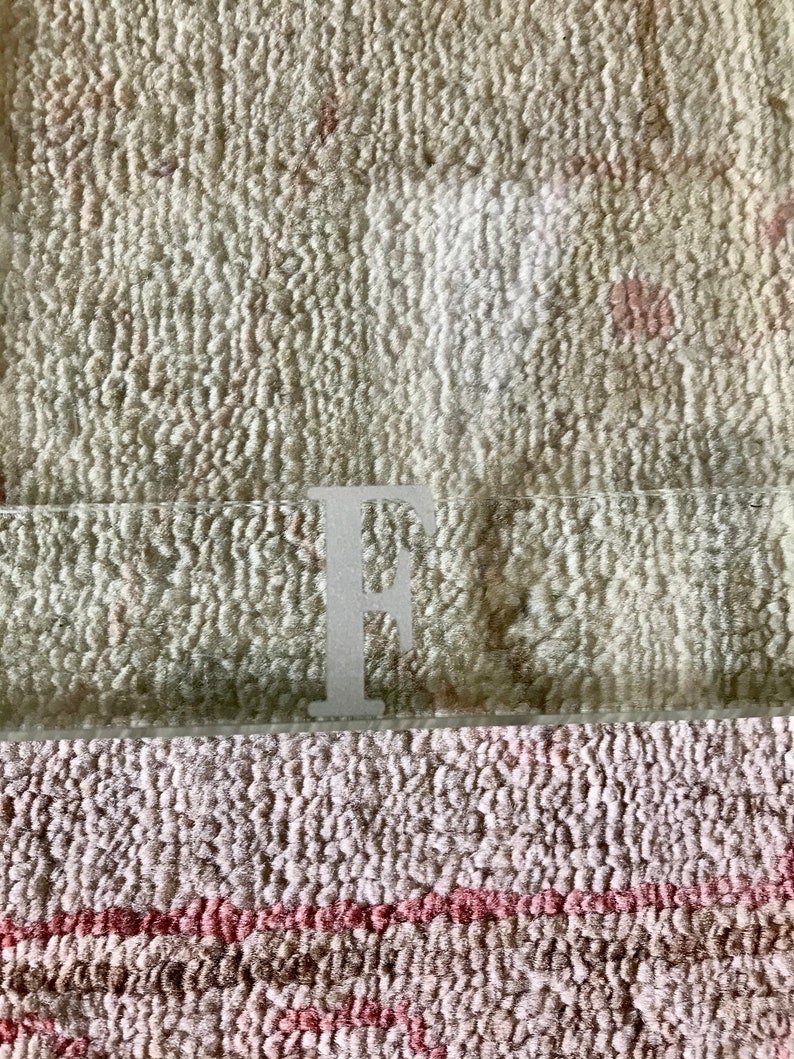 May include: A clear glass tray with the letter "F" etched on the bottom. The tray is sitting on a beige and pink patterned rug.