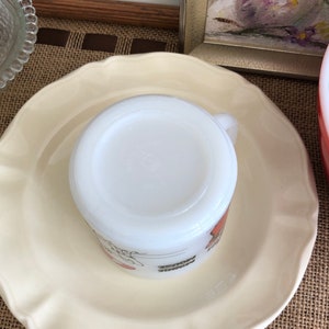 May include: White ceramic mug with a red and orange design. The mug is sitting on a white saucer.