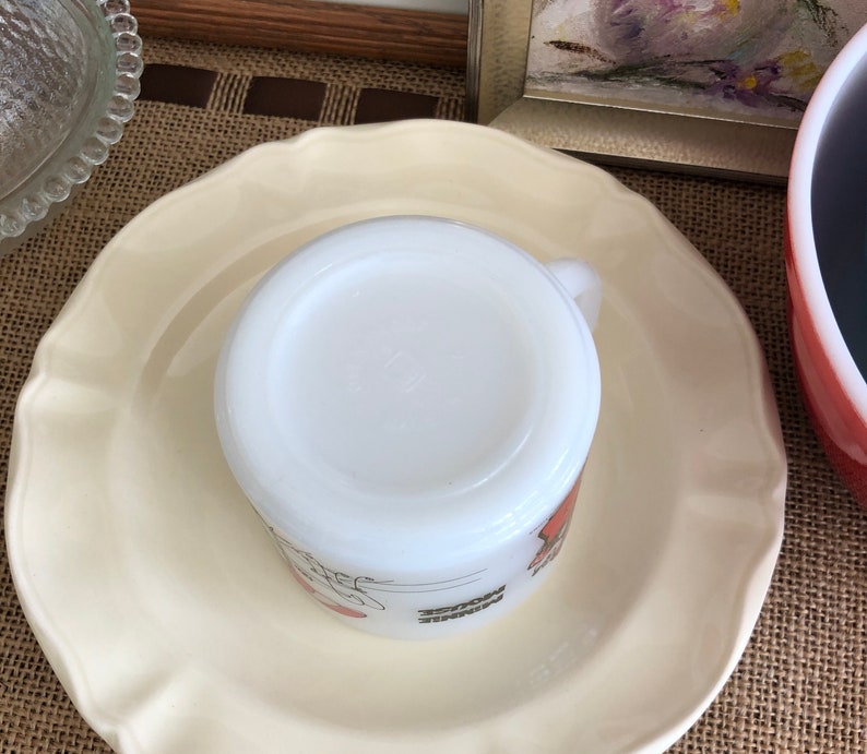 May include: White ceramic mug with a red and orange design. The mug is sitting on a white saucer.