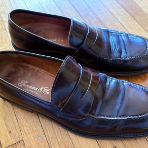 May include: A pair of dark brown leather penny loafers with a square toe design and visible stitching along the vamp. The interior insoles are stamped with the text "Faramocca & Co" and "MADE IN ITALY" in a white script and block font.