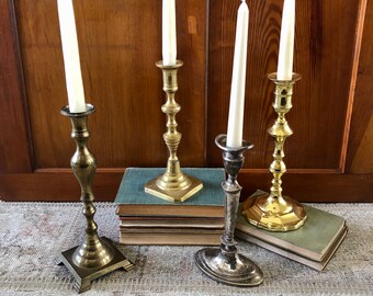 May include: Four candle holders, two gold and two silver, with white candles. The candle holders are on a stack of books with a patterned rug underneath.
