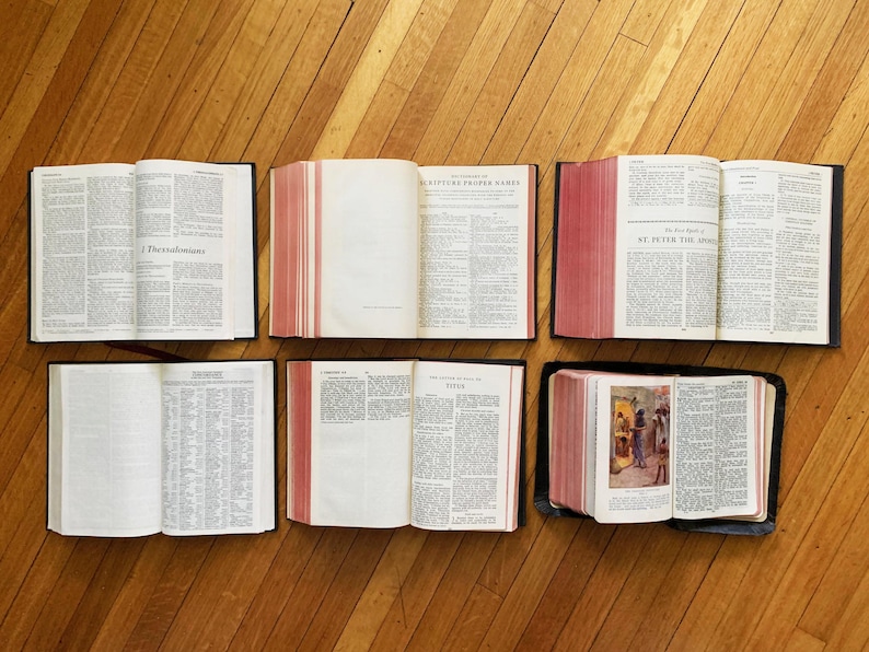 May include: Six open books with black covers and red edges. The books are laid out on a wooden floor. The titles of the books are visible: "I Thessalonians", "Scripture Proper Names", "St. Peter the Apostle", "Titus", and "The Acts of the Apostles".