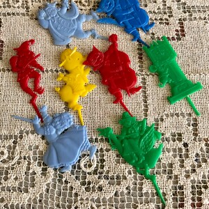 May include: A set of nine colorful plastic cake toppers featuring characters from the Wizard of Oz. The toppers include Dorothy, the Scarecrow, the Tin Man, the Cowardly Lion, the Wicked Witch of the West, the Wizard, and the flying monkeys. The toppers are perfect for a Wizard of Oz themed party.