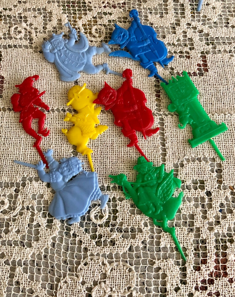 May include: A set of nine colorful plastic cake toppers featuring characters from the Wizard of Oz. The toppers include Dorothy, the Scarecrow, the Tin Man, the Cowardly Lion, the Wicked Witch of the West, the Wizard, and the flying monkeys. The toppers are perfect for a Wizard of Oz themed party.