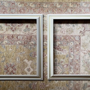 May include: Two white picture frames with gold trim, both are empty and set against a patterned background.