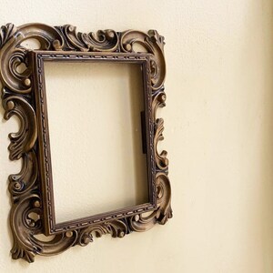 May include: A gold ornate picture frame with a detailed design. The frame is empty and ready for a picture.