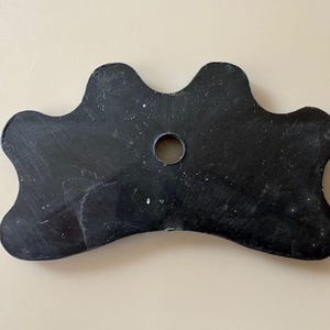 K&ouml;nnte beinhalten: Ein schwarzer Billardqueue-Br&uuml;ckenhalter mit gewelltem Rand und einem zentralen Loch. Der Br&uuml;ckenhalter besteht aus einem soliden, dunklen Material und hat eine glatte, leicht abgenutzte Oberfl&auml;che. Das Design ist symmetrisch, mit drei gebogenen Abschnitten auf jeder Seite.