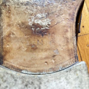 May include: The tan leather sole of a shoe featuring a worn texture and visible markings. The number 10.5 is embossed in the center of the sole, positioned above the letter M, indicating the size and width of the footwear clearly visible.