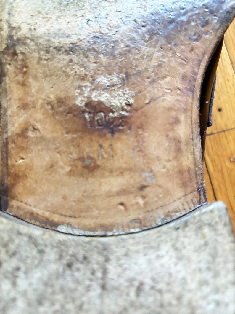 May include: The tan leather sole of a shoe featuring a worn texture and visible markings. The number 10.5 is embossed in the center of the sole, positioned above the letter M, indicating the size and width of the footwear clearly visible.