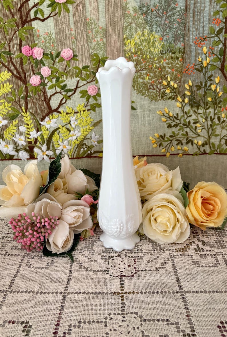 Peut inclure: Un vase blanc de style vintage avec un dessus festonn&eacute; et une base d&eacute;taill&eacute;e. Le vase est entour&eacute; de roses cr&egrave;me et p&ecirc;che et de fleurs roses. L'arri&egrave;re-plan pr&eacute;sente une tapisserie florale brod&eacute;e.