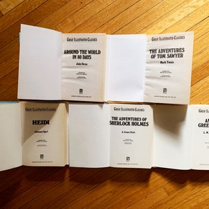 May include: Six classic literature books with white covers and black text. The titles are "Around the World in 80 Days", "The Adventures of Tom Sawyer", "Heidi", "The Adventures of Sherlock Holmes", and "Anne of Green Gables".