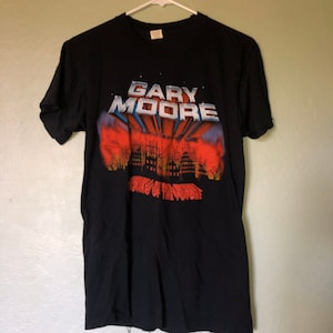以下が含まれることがあります： Gary Mooreのアルバム「After the War」のジャケットがプリントされた黒いTシャツ。グラフィックは炎に包まれた街並みと「Gary Moore」と「After the War」の文字が描かれている。