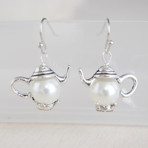 Peut inclure: Une paire de boucles d'oreilles en forme de théière argentée avec des accents de perles blanches. Les boucles d'oreilles ont un design délicat et sont parfaites pour ajouter une touche de fantaisie à n'importe quelle tenue.