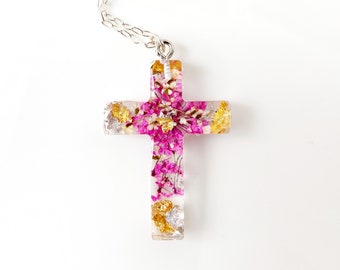 May include: A silver chain necklace with a pink and gold cross pendant. The cross is filled with pressed flowers and gold flakes.