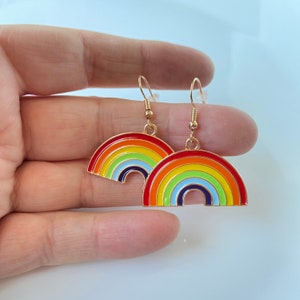 May include: A pair of gold rainbow earrings. Each earring features a rainbow arch with red, orange, yellow, green, blue, indigo, and violet enamel.