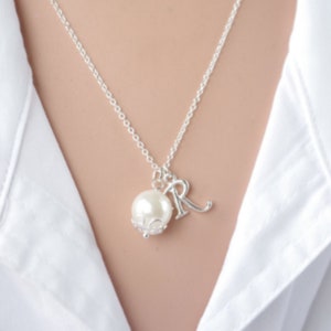 Puede incluir: Un collar de cadena de plata con una perla y un dije de plata con la letra "R" colgando.