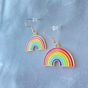 May include: A pair of gold-tone rainbow earrings. Each earring features a rainbow arch with red, orange, yellow, green, blue, indigo, and violet enamel.