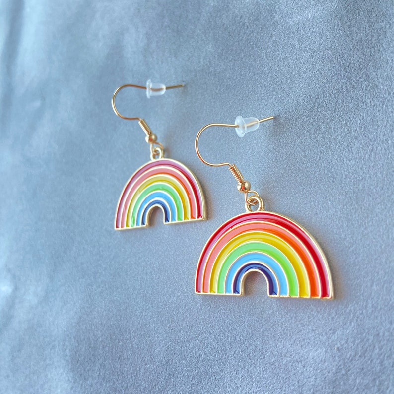 May include: A pair of gold-tone rainbow earrings. Each earring features a rainbow arch with red, orange, yellow, green, blue, indigo, and violet enamel.
