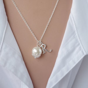 Puede incluir: Un collar de cadena de plata con una perla y un dije de plata con la letra "R" colgando.