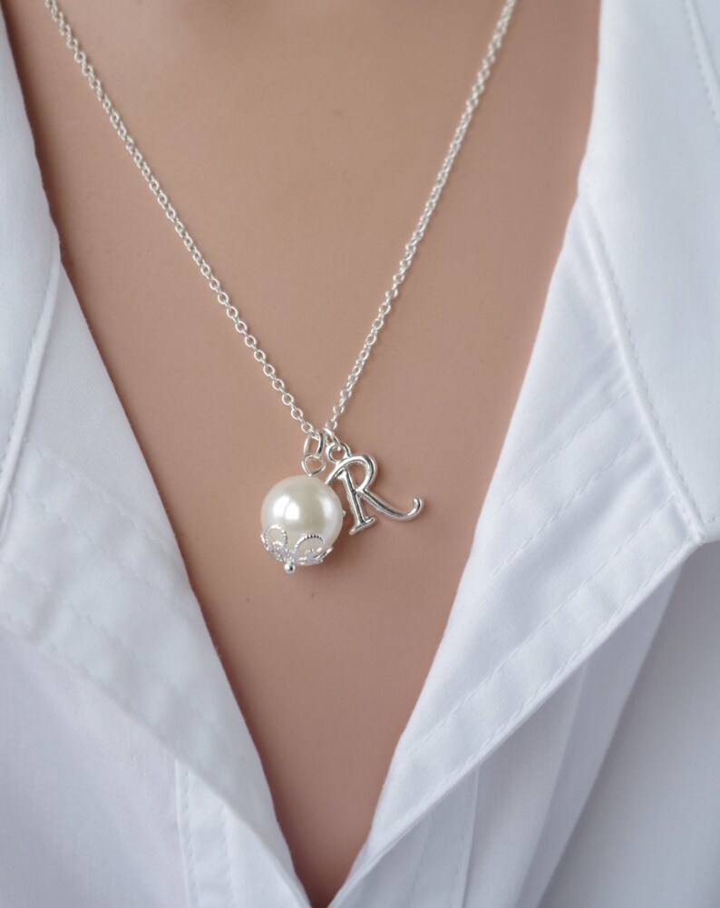 Puede incluir: Un collar de cadena de plata con una perla y un dije de plata con la letra "R" colgando.