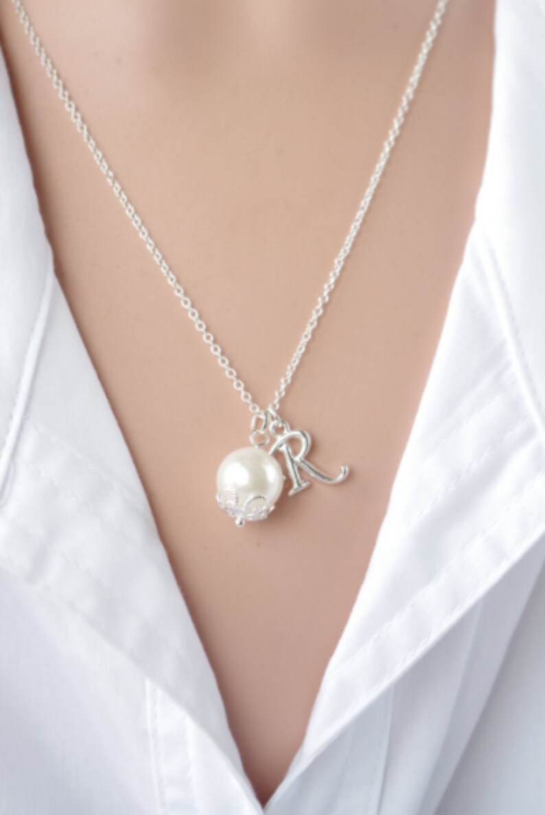 Puede incluir: Un collar de cadena de plata con una perla y un dije de plata con la letra "R" colgando.