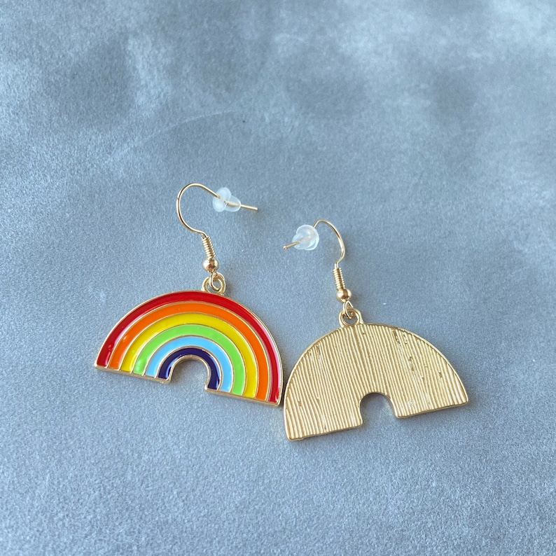 May include: A pair of gold-tone earrings with a rainbow design. One earring is a rainbow arch with red, orange, yellow, green, blue, indigo, and violet enamel. The other earring is a solid gold arch.