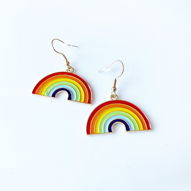 May include: A pair of rainbow-coloured earrings with gold hooks. Each earring features a rainbow arch with red, orange, yellow, green, blue, indigo, and violet enamel.