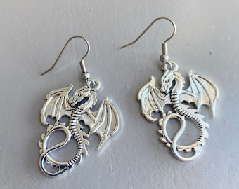 Peut inclure: Une paire de boucles d'oreilles en argent en forme de dragon avec des ailes détaillées et une queue enroulée. Les boucles d'oreilles sont sur un crochet en argent.