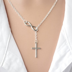 May include: A silver necklace featuring an infinity symbol and a cross pendant.