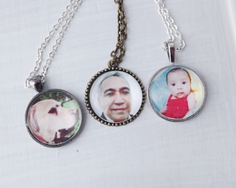May include: Three silver necklaces with round glass pendants featuring photos of a man, a baby, and a dog. The pendants are attached to silver chains.