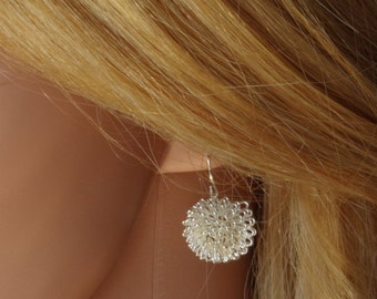 May include: Silver dangle earrings with a round, textured, silver charm. The charm is made of many small, interconnected loops.
