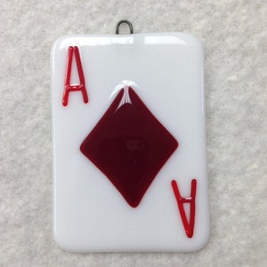 May include: A glass ornament shaped like a playing card, featuring the Ace of Diamonds. The card is white with a red diamond and red 'A's on each corner.