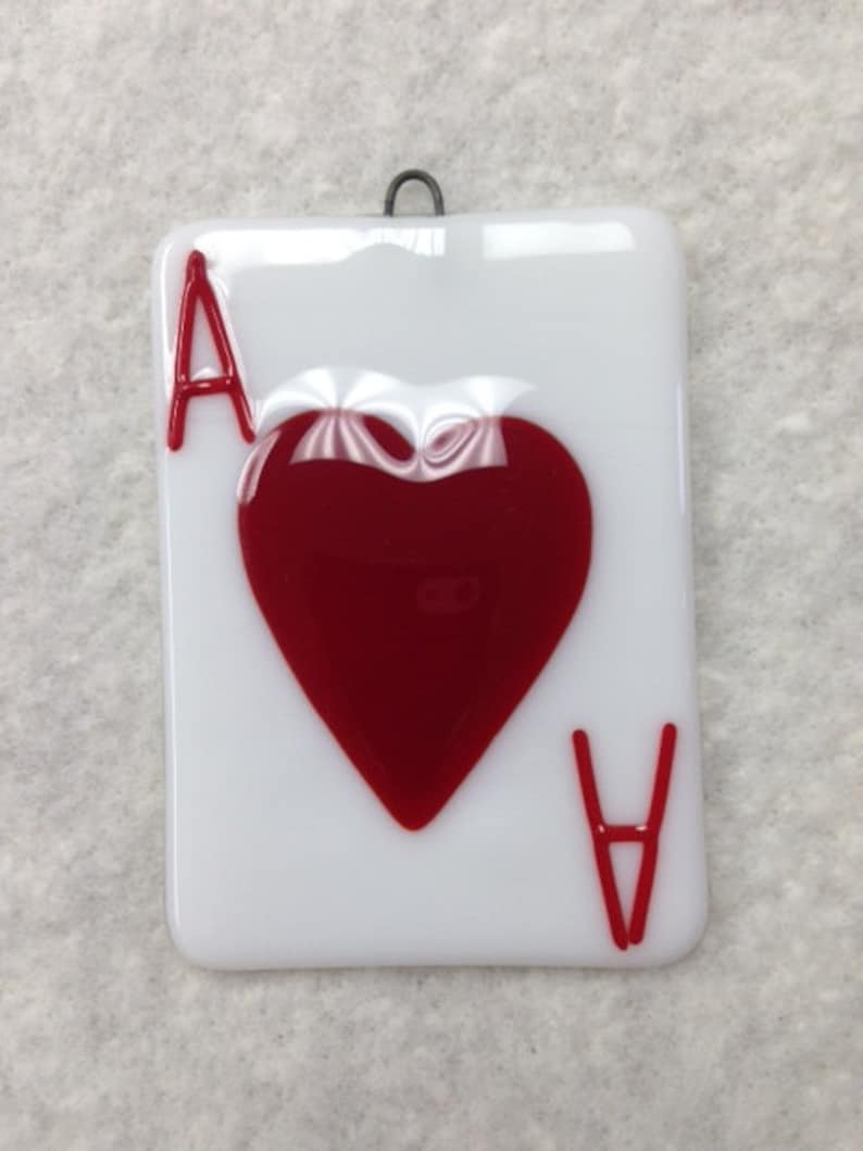 May include: A white glass ornament shaped like a playing card with a red heart and the letter 'A' on it.