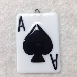 May include: A white glass ornament with a black ace of spades design. The ornament has a metal hanger.