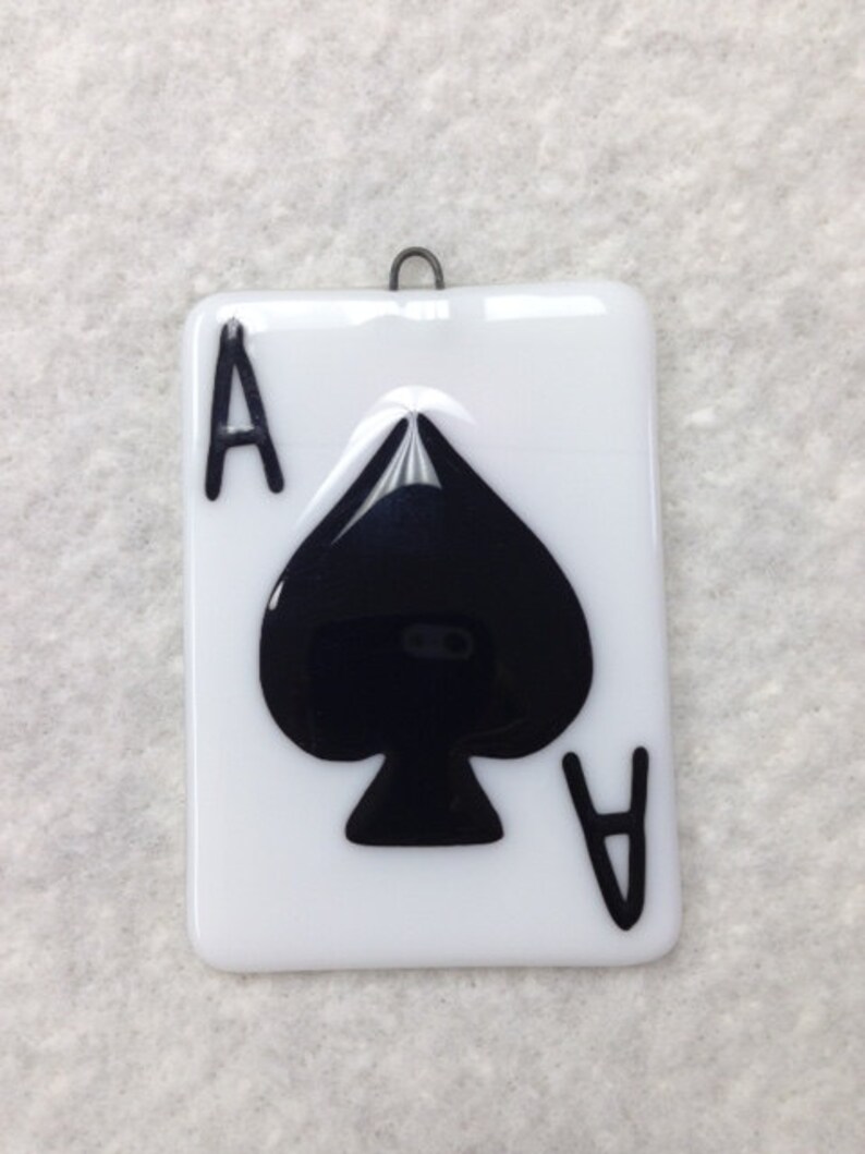 May include: A white glass ornament with a black ace of spades design. The ornament has a metal hanger.