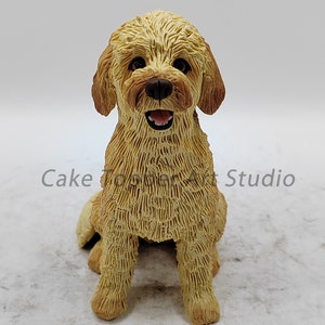 Może przedstawiać: Mała figurka psa w kolorze kremowym z brązowymi akcentami futra. Pies siedzi z głową uniesioną do góry i lekko otwartą paszczą, jakby się uśmiechał. Figurka wykonana jest z fakturowanego materiału przypominającego futro.