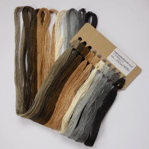 Könnte beinhalten: Ein Set mit 16 Stickgarn-Knäuel in verschiedenen Brauntönen, Beige, Grau und Schwarz. Die Knäuel sind auf einer Pappekarte mit dem Text "CLASSIC NEUTRALS" und "www.paintboxthreads.co.uk" angeordnet.