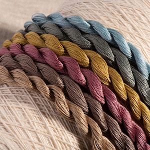 May include: A collection of embroidery floss spools in various shades of brown, beige, and blue. The floss is arranged in a rainbow pattern, with the lightest colours at the top and the darkest colours at the bottom.
