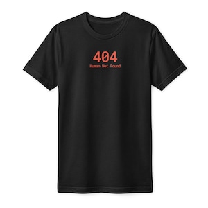 May include: A black short-sleeved t-shirt featuring the text 404 and the phrase Human Not Found printed in a reddish-orange colour on the centre of the chest. The garment has a standard crew neckline and a straight hemline at the bottom.