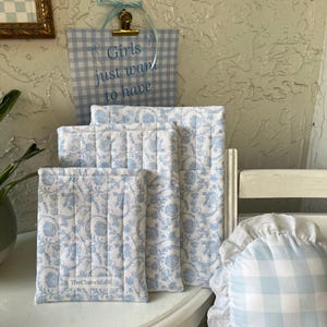 Może przedstawiać: Cztery kwadratowe kawałki tkaniny pikowanej w kolorze niebieskim i białym z kwiatowym wzorem. Kwadraty są ułożone jeden na drugim i mają etykietę z napisem "TheChaveliEdit".