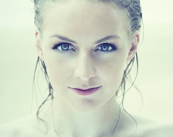 May include: A close-up portrait of a woman with wet, blonde hair. She has blue eyes and is wearing a silver necklace.