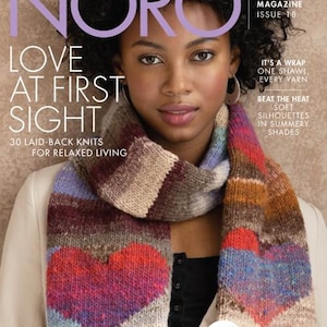 May include: A woman wearing a colorful knitted scarf with a heart design. The scarf is made of various shades of purple, red, blue, and brown. The magazine cover reads "NORO LOVE AT FIRST SIGHT" and "KNITTING MAGAZINE ISSUE 18".