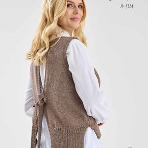 May include: A brown sleeveless knitted vest with a tie at the back. The vest is worn over a white shirt and blue jeans. The text "JUNE" and "JL-5224" is printed on the image. The text "Jody Long Coastline Collection" is also printed on the image.
