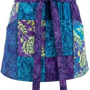 May include: A colorful patchwork apron with a tie waist. The apron features a mix of blue, purple, and green floral and abstract patterns. It has two pockets and a tie closure. The apron is designed for kitchen or craft use.