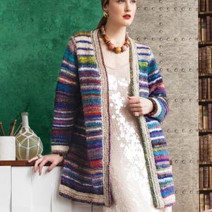 Könnte beinhalten: Ein langer, offener Cardigan mit einem lebendigen Streifenmuster aus Blau, Lila, Rot und Grün. Der Pullover hat eine cremefarbene Bordüre und wird über einem paillettenbesetzten Kleid getragen. Das Design des Cardigans weist eine Mischung aus Farben und Texturen auf.