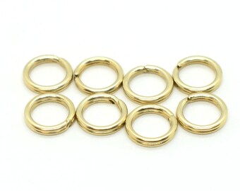 May include: Eight gold jump rings, also known as split rings, are arranged in a row on a white background. These rings are commonly used in jewelry making and crafting.