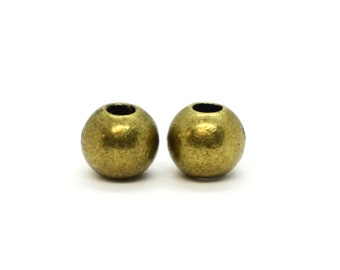 May include: Two round, antique brass beads with a textured surface and a hole through the center. These beads are ideal for jewelry making and crafting projects. The beads are set against a white background.