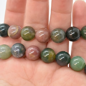 May include: A strand of green, brown, and pink agate beads. The beads are round and smooth, and they are strung on a clear elastic cord.