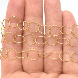 May include: A gold chain made of oval-shaped links. The chain is lying on a hand, with the links overlapping.