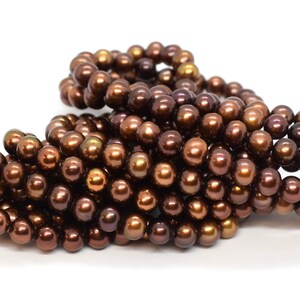 May include: A strand of brown freshwater pearls. The pearls are round and have a slight iridescent sheen.